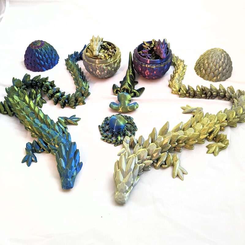 A flat-lay of finished articulated dragon and creature prints in iridescent filament, plus dragon-egg containers