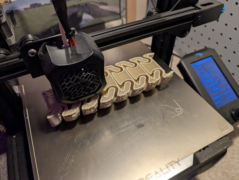 A 3D printer mid-print on a flexible articulated piece in cream-colored filament