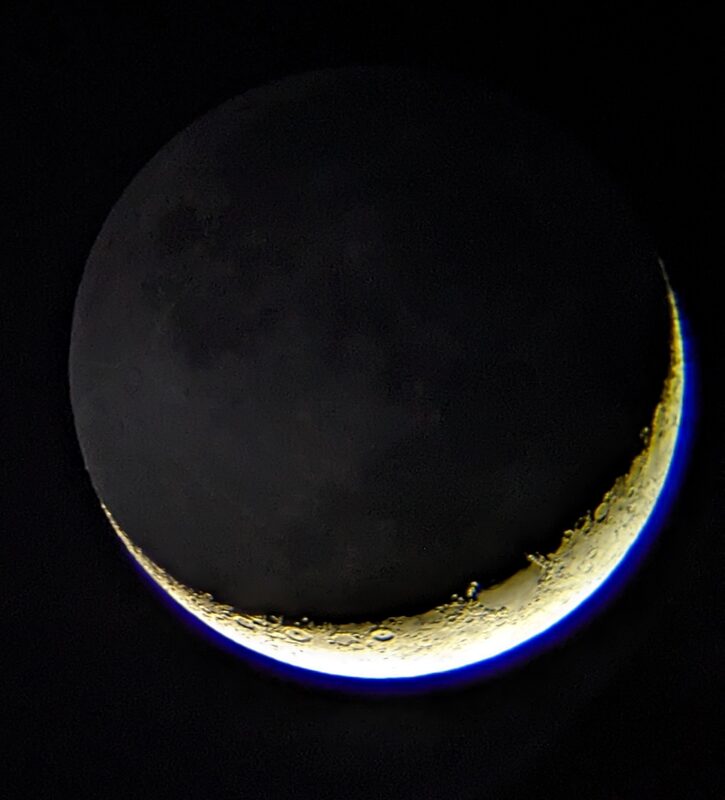 A crescent moon with earthshine faintly lighting the dark portion of the disk