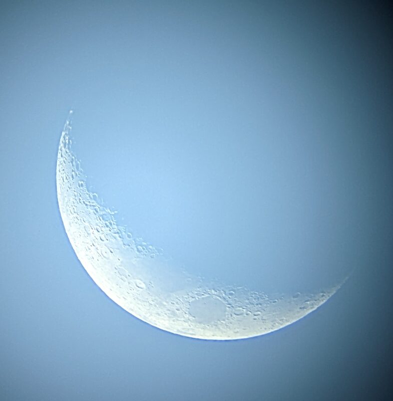 A sharp crescent moon against a clear blue sky