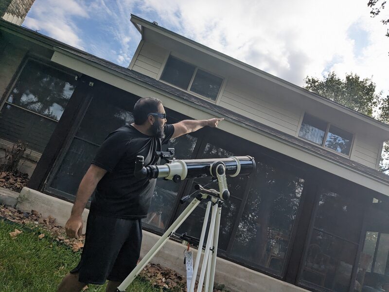 Me wearing eclipse glasses next to the Celestron telescope, pointing at the sky, on eclipse day