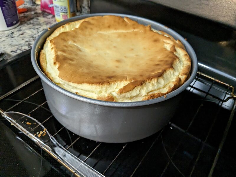 A cheesecake, puffed and golden, in a springform pan in the oven