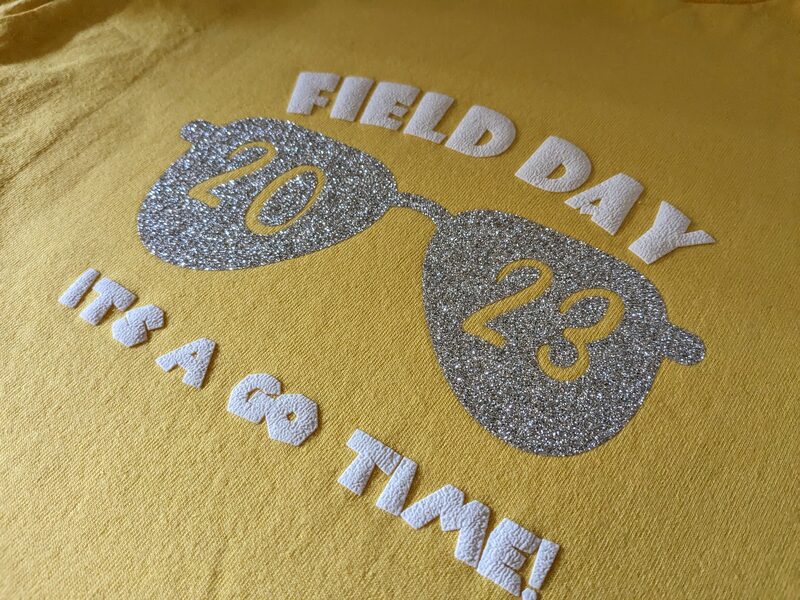 A yellow shirt with a glittery iron-on Field Day 2023 design