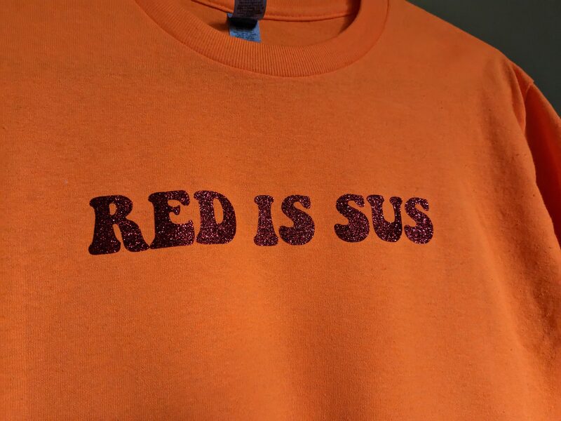 An orange shirt with a glittery Red Is Sus iron-on design