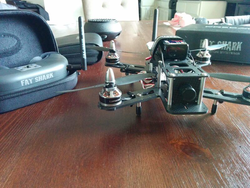 The fully assembled racing drone with an FPV camera mounted, Lumenier motors, next to the Fat Shark goggles case