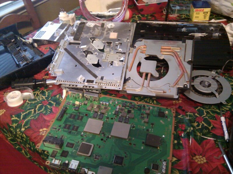 A PS3 fully disassembled on a table - motherboard, heatsink with copper heat pipes, fan, disc drive, and power supply, laid out for a Yellow Light of Death repair