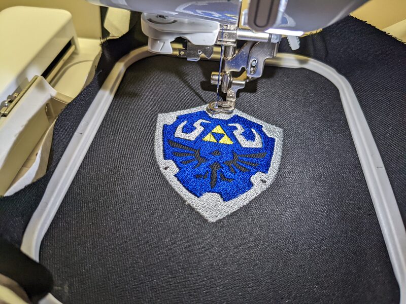 A Hylian Shield patch from Legend of Zelda, mid-final-stitch in the machine hoop