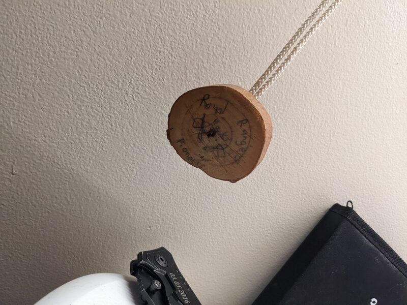 A wood-slice pendant hand-inked with Royal Rangers Pioneers, hanging on a paracord cord