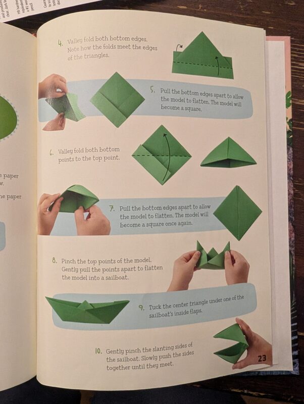 An origami instruction book open to a page showing step-by-step folds for a sailboat
