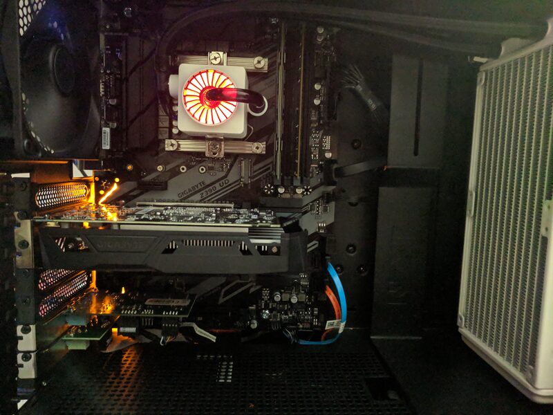 Inside the same PC build, an earlier shot showing a Gigabyte Z390 motherboard, a lit liquid CPU cooler pump, and a Gigabyte GPU