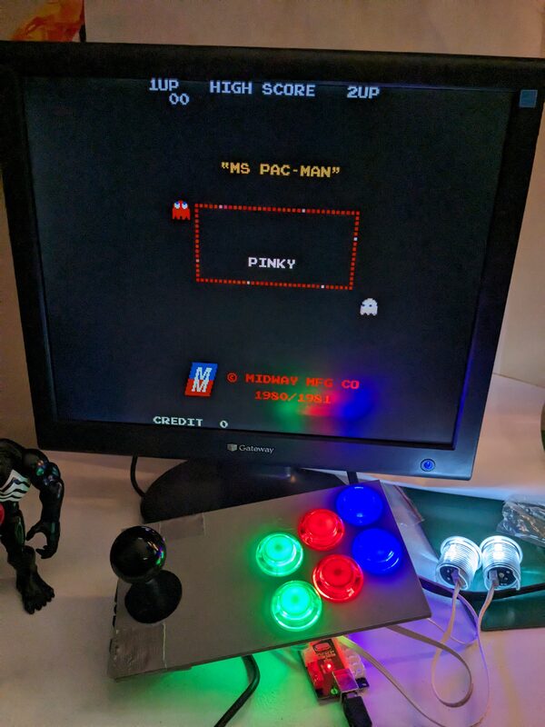 An early 3D printed arcade controller prototype with a joystick and lit buttons, wired to a Raspberry Pi, with Ms. Pac-Man running on the monitor behind it