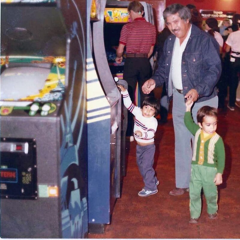 My grandpa holding hands with my cousin Nick and me as kids, walking through an arcade full of cabinets in the 1980s