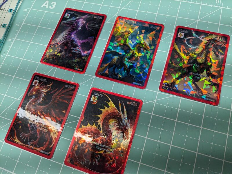 Five finished holographic dragon and phoenix cards, each named with custom HP, moves, and a print number