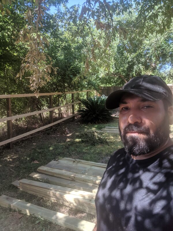 A selfie next to the repaired wood fence, new pickets and framing visible