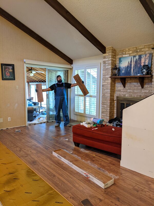 Installing Pergo laminate flooring in a living room with a stone fireplace, holding a plank overhead